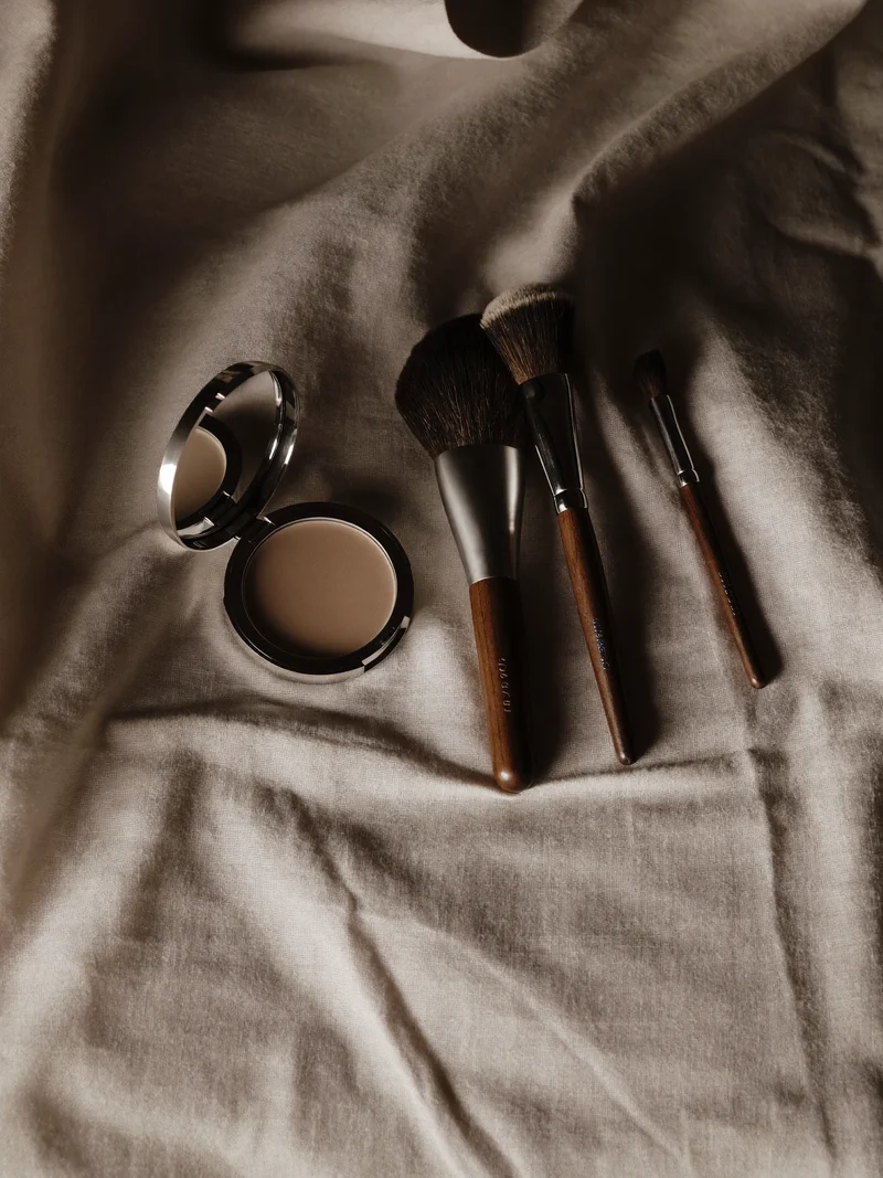 Pinceaux à poils naturels et poudre compacte vierge sur un tissu de lin clair